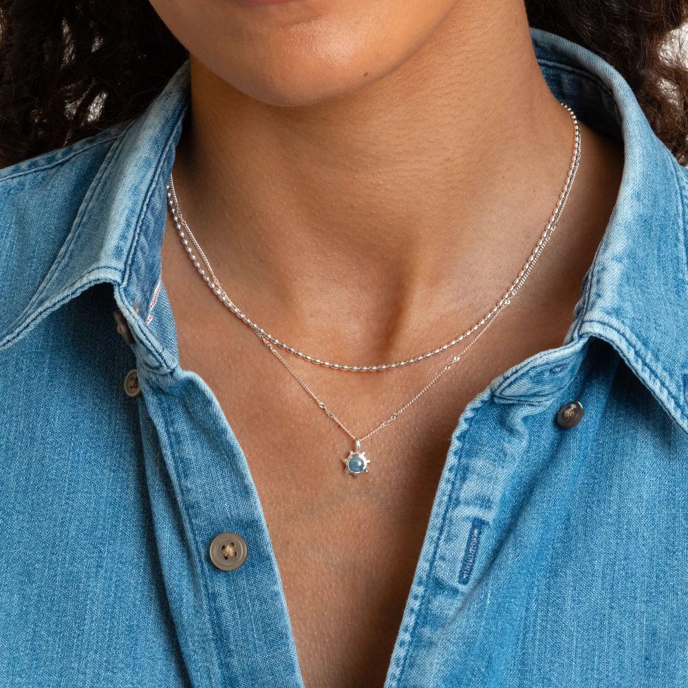 Syster P Lunetta halsband silver, enkelt kedjehalsband med små ovala länkar, stylat i lager med ett halsband med blå sten mot denimskjorta.