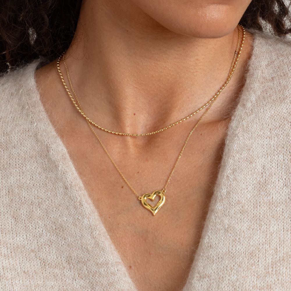 Syster P Lunetta halsband guld, kedja med små ovala länkar i 18 K guldplätering, stylat i lager med ett hjärthalsband mot beige stickad tröja.