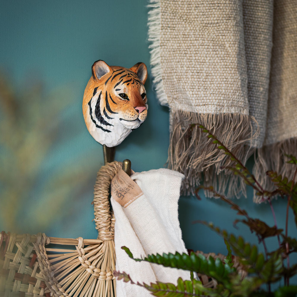 Hook Tiger mounted on a wall in a hallway setting, holding a towel and a woven fan.