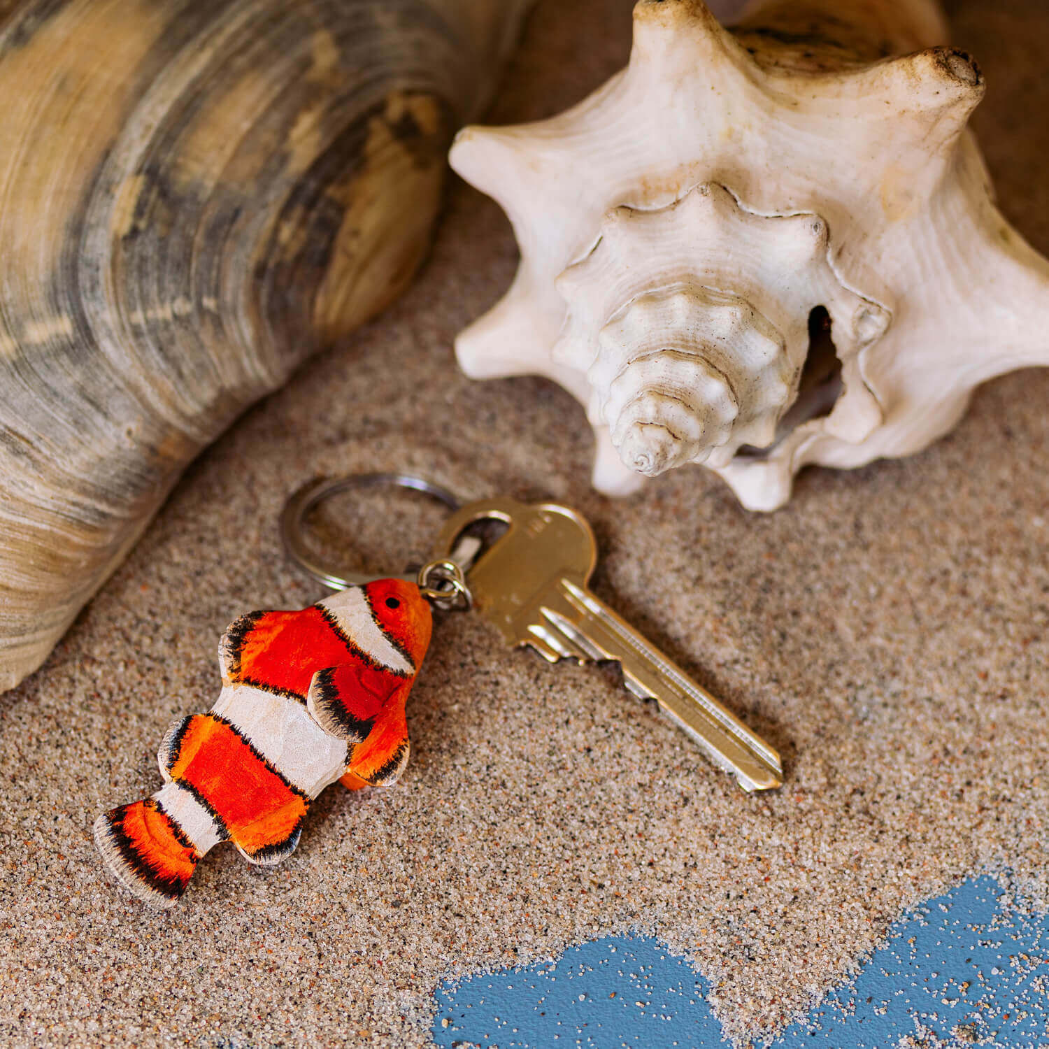 Porte-clés Poisson-clown posé sur du sable à côté de coquillages.
