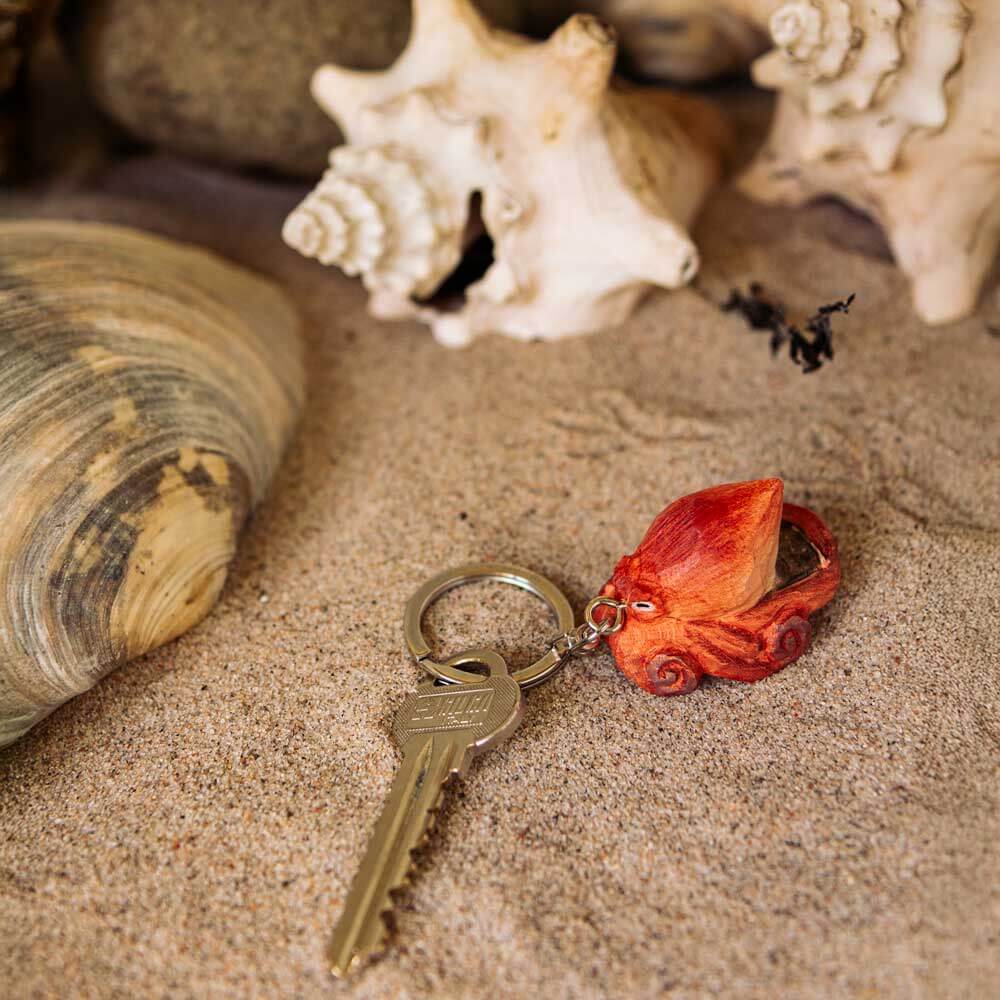Porte-clés Poulpe posé sur du sable parmi des coquillages.