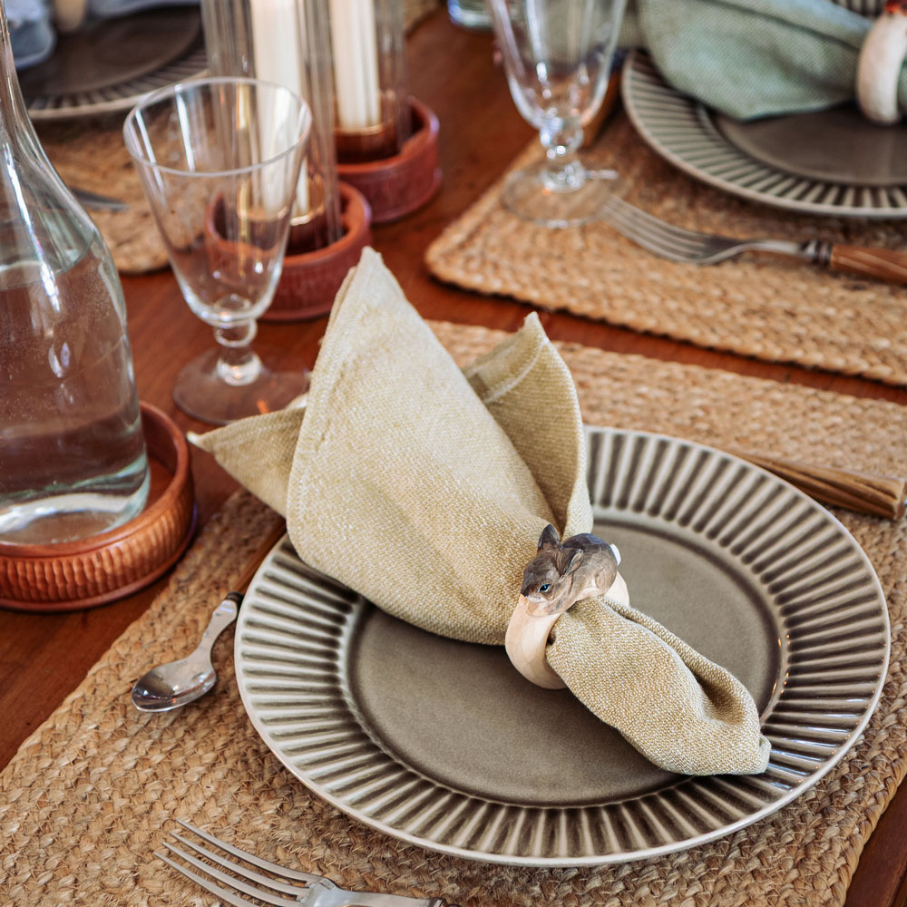 Gros plan d’une table dressée avec le Rond de serviette – Lapin Mini autour d’une serviette beige sur une assiette grise.