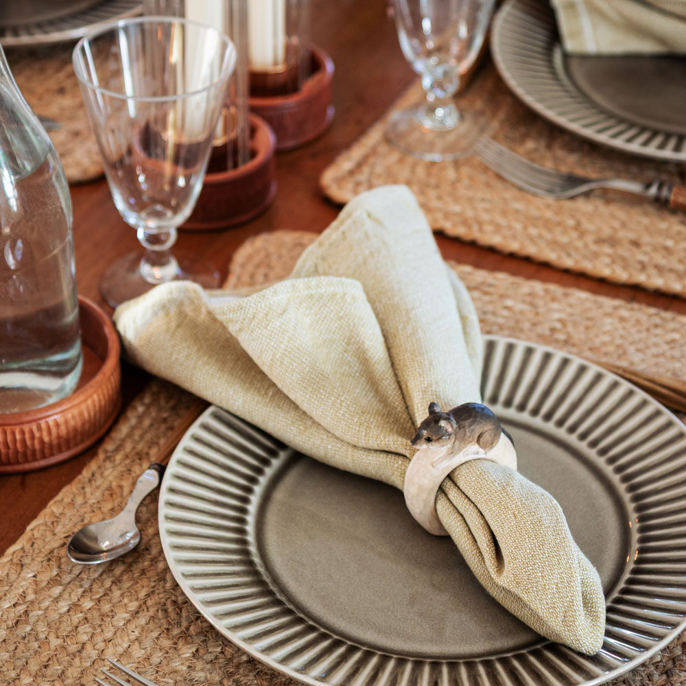 Gros plan d’une table dressée avec le Rond de serviette – Souris Mini autour d’une serviette beige sur une assiette grise.