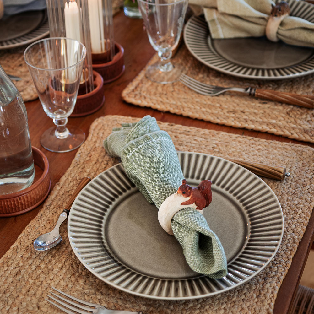 Gros plan d’une table dressée avec le Rond de serviette – Écureuil Mini autour d’une serviette verte sur une assiette grise.