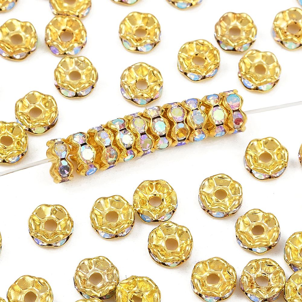Strassrondell Clear A, rund 6 mm rhinestone-rondell i gyllene metallfärg med iriserande AB-stenar, visad i närbild på rad på en nål samt utspridda runtom.