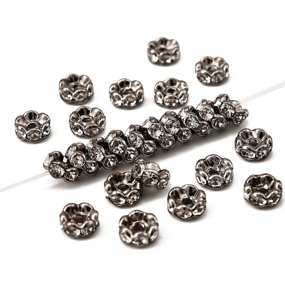 Nickelfria gunmetal-rondeller med vågig kant och infattade klara kristaller, 6×3 mm, visade i närbild utspridda och trädda på tråd
