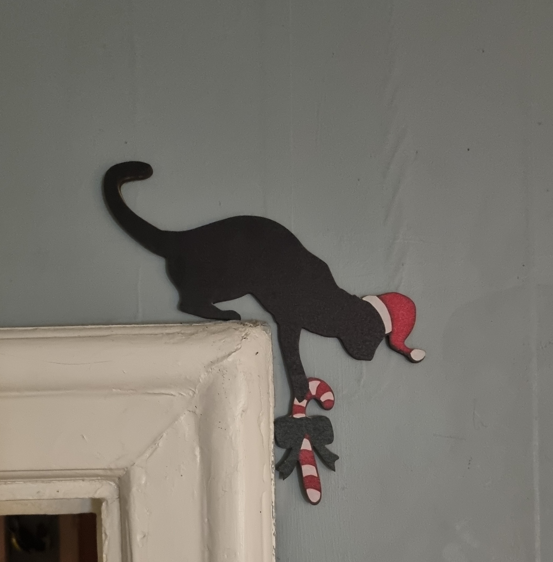 Skylt i träfaner att sätta ovanför dörrfodret "Julkatt med polkagris"