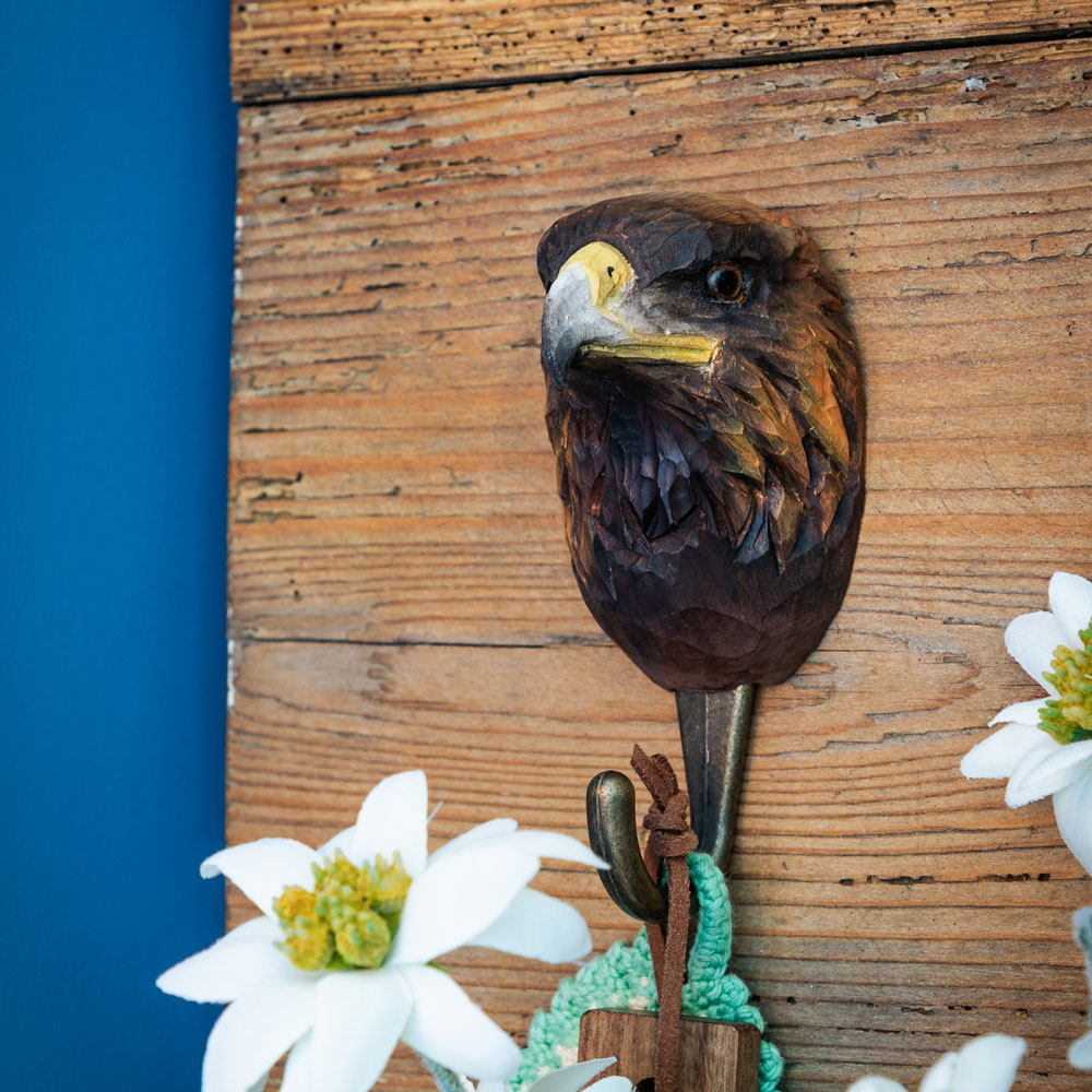 Patère sculptée à la main avec aigle royal fixée sur un mur en bois rustique, avec moufles tricotées et peau de mouton en arrière-plan.