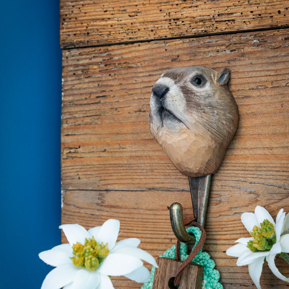 Patère sculptée à la main avec marmotte fixée sur un mur en bois rustique, avec détail en peau de mouton et tissu suspendu.