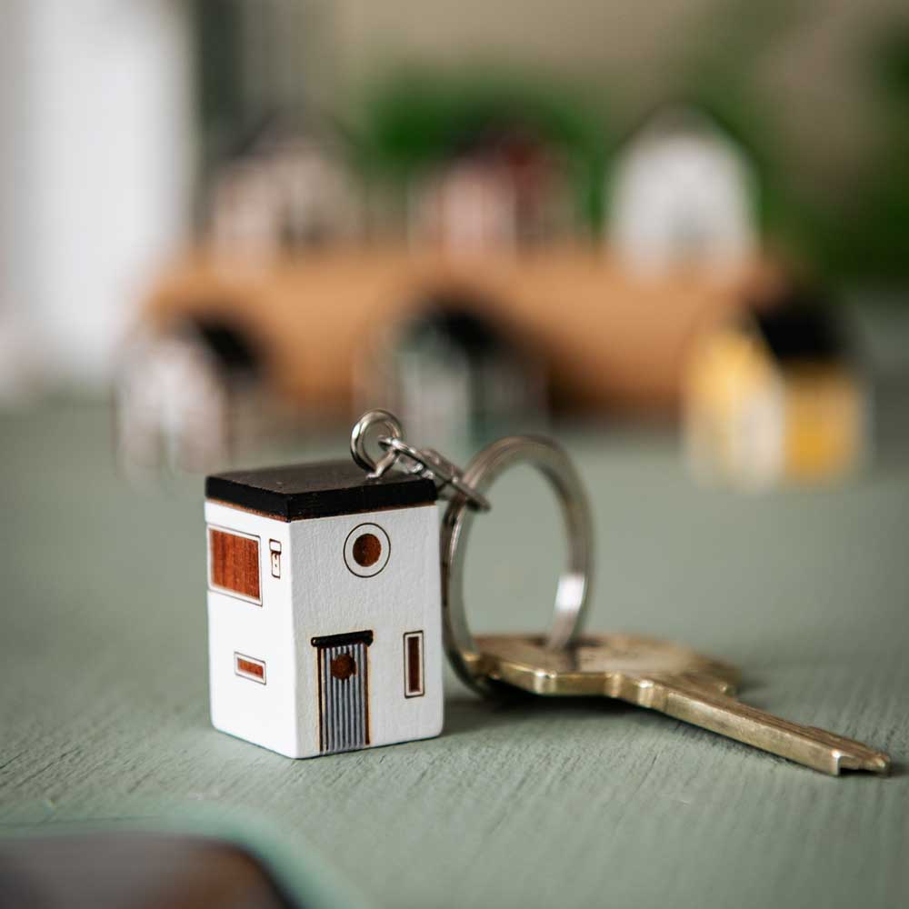 Porte-clés Maison Moderne posé à côté de clés sur une table, avec de petites maisons en arrière-plan.