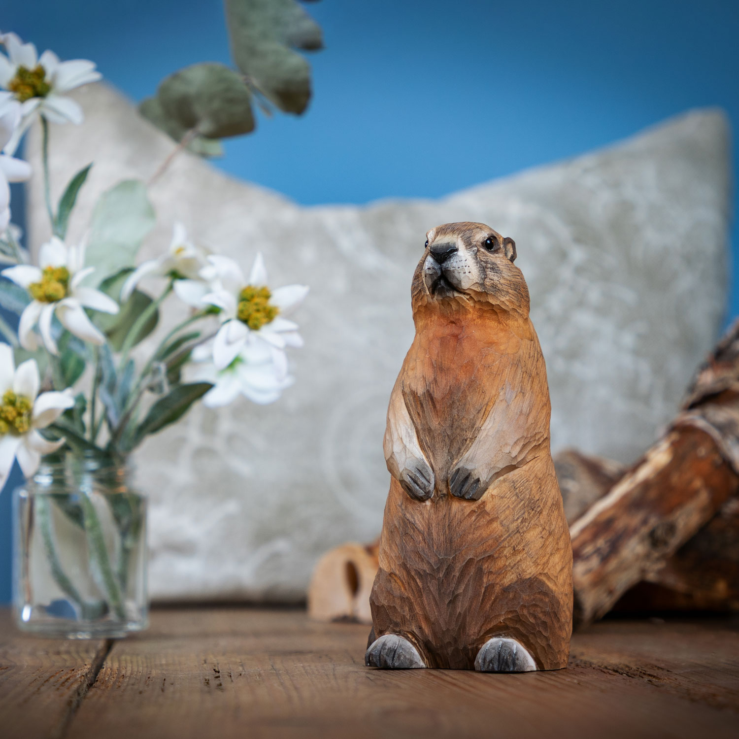 Marmotte sculptée à la main posée sur une table en bois à côté de fleurs blanches et de branches en bois.