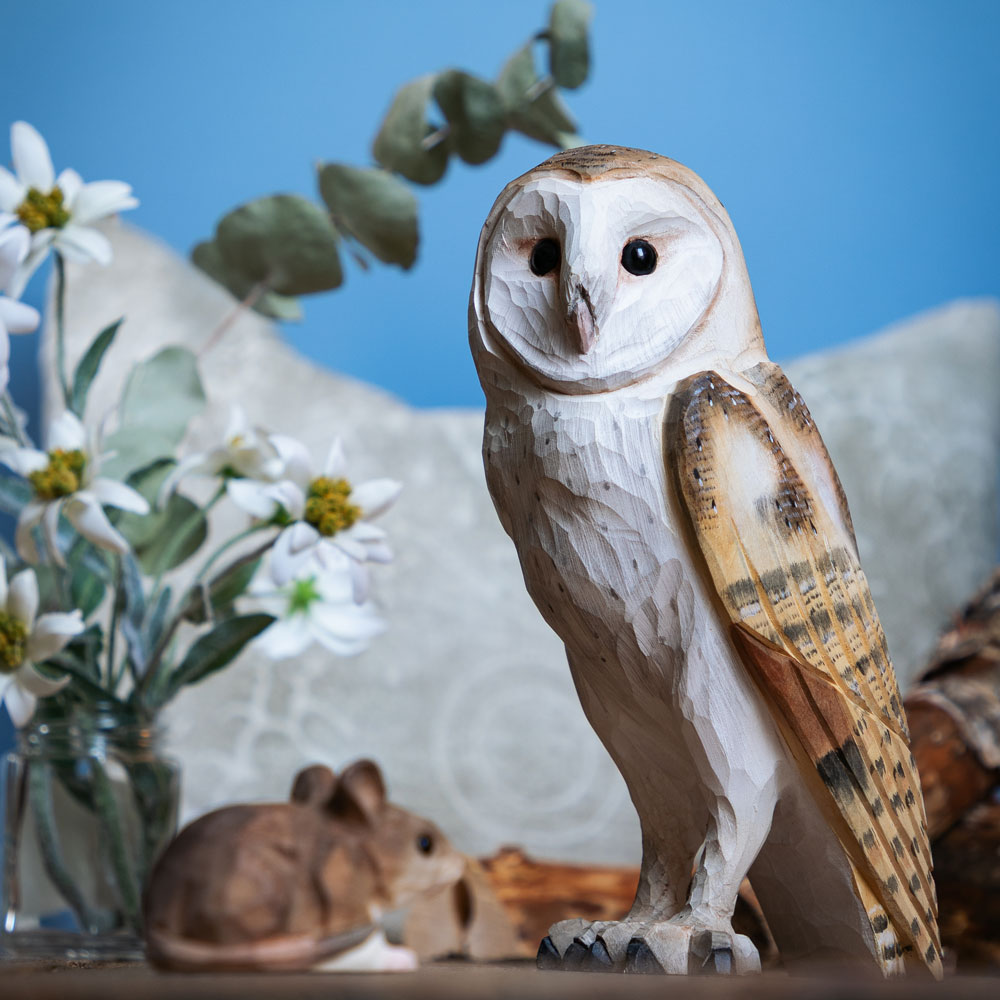Hand-carved barn owl in wood beside firewood and soft winter lights.