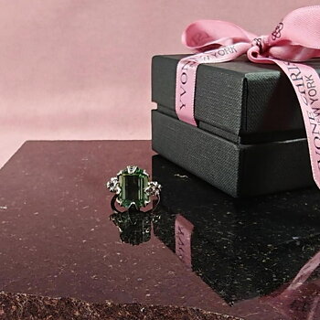 Yvone Christa Menage Square ring i sterling silver med stor fyrkantigt slipad grön Aqua Lemurian-sten, placerad på en mörk stenskiva bredvid en svart presentask med rosa band.