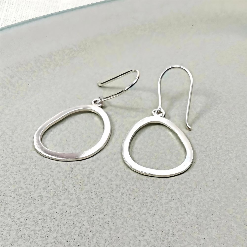 IAMLUND Glänta örhänge silver, blankt, öppet ovalt örhänge ca 45 mm, visas i närbild med organisk form.