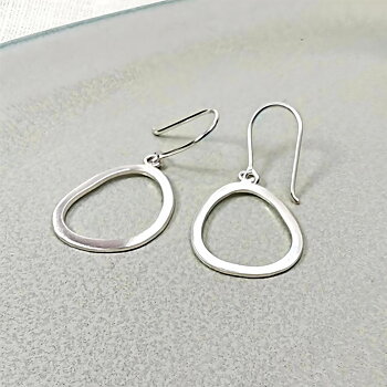 IAMLUND Glänta örhänge silver, blankt, öppet ovalt örhänge ca 45 mm, visas i närbild med organisk form.