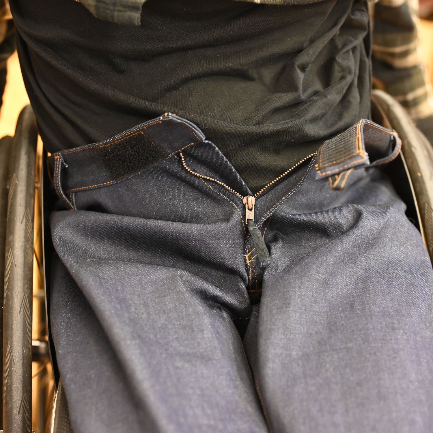 Dark blue wheelchair jeans on a person sitting in a wheelchair; 100% organic cotton; close-up of the open fly