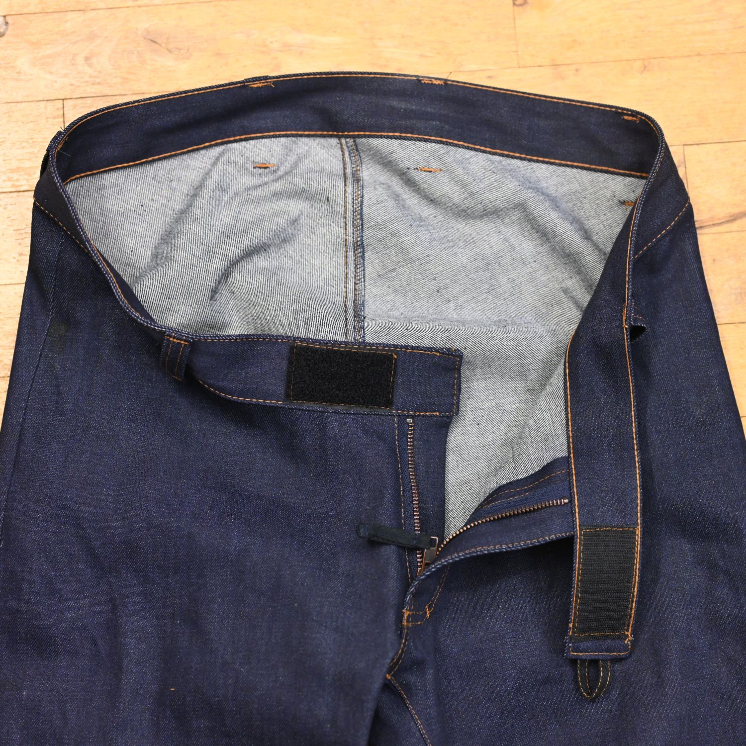 Dark blue wheelchair-accessible jeans on a person sitting in a wheelchair; 100% organic cotton; close-up of the open fly on the floor