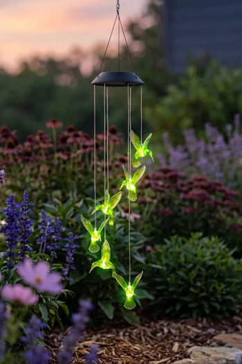 Solkolibri lyser grönt i skymningen bland lavendel, cosmos och rudbeckia i en rabatt