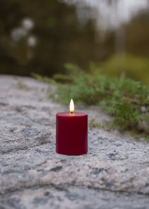 Ett rött batteridrivet LED-blockljus med verklighetstrogen låga, stående utomhus på en grå sten i naturen.