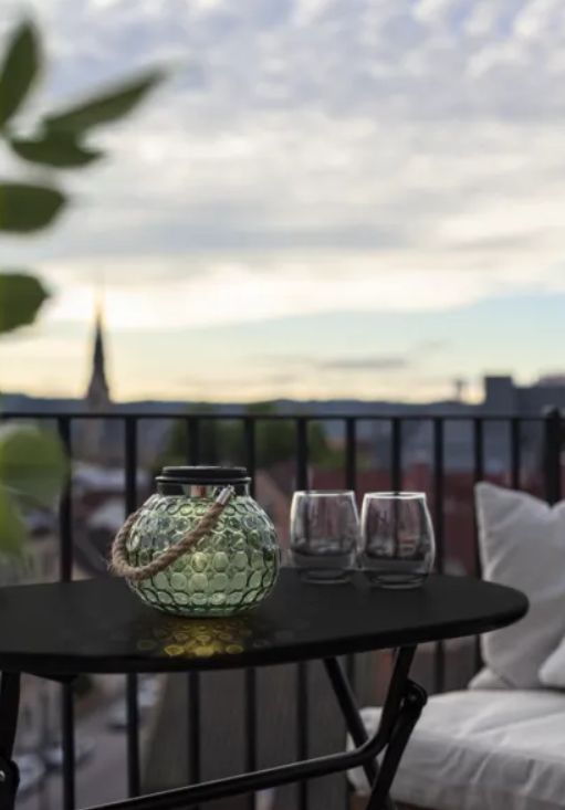 Green glass solar lantern glowing on a black balcony table overlooking a city skyline at dusk.