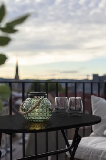 Grön solcellslykta i glas lysande på ett svart balkongbord med utsikt över staden i skymningen.