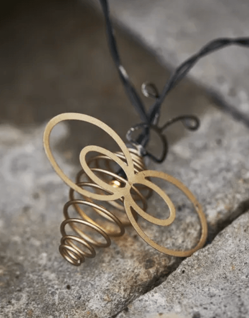 Close-up of a decorative gold metal wire bee from an outdoor solar string light resting on a stone surface.