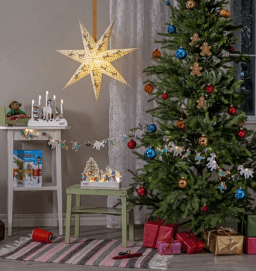 Pippi Longstocking themed Christmas decorations including a hanging advent star, string lights, and ornaments next to a decorated Christmas tree.