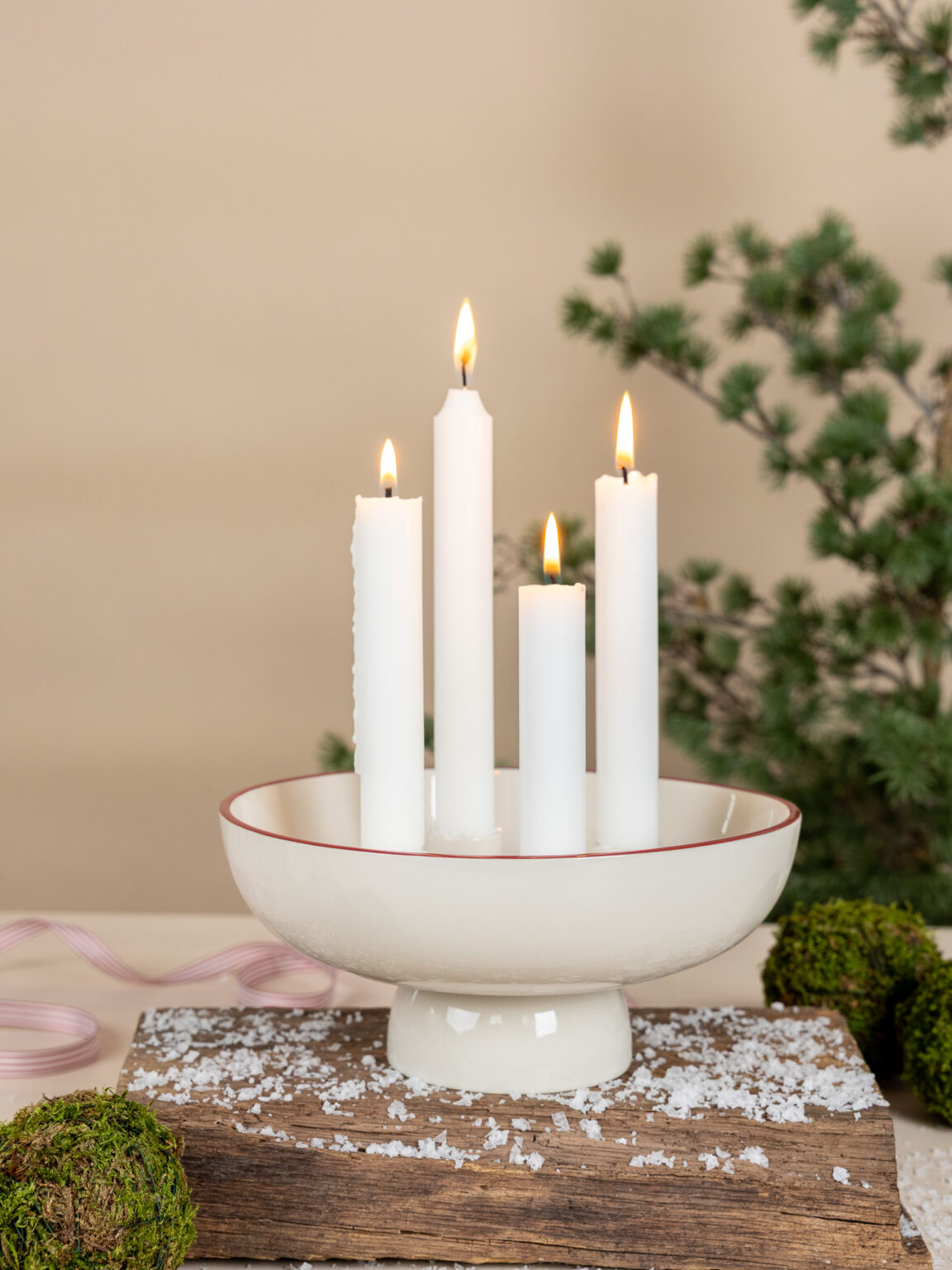 Vacker juldekoration med adventsljusstaken Granhammar Jubileum. Skålen i vit keramik rymmer fyra levande ljus som brinner stämningsfullt omgivna av snö, mossa och tallkvistar.