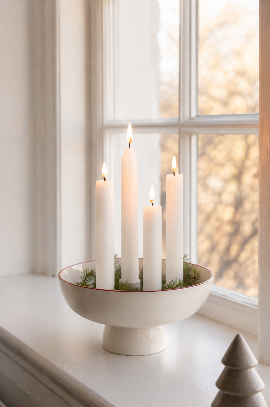 Tänd vit adventsljusstake i keramik från Storefactory, modell Granhammar Jubileum, dekorerad med granris på en ljus fönsterbräda.