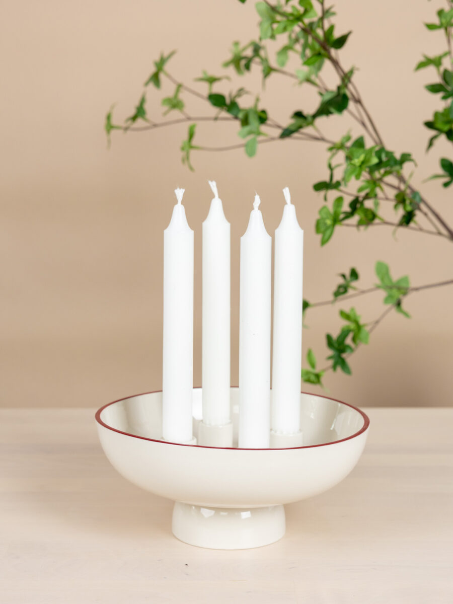 Osläckt vit adventsljusstake på fot i keramik med tunn röd kant, Granhammar Jubileum, stilrent placerad på ett ljust träbord.