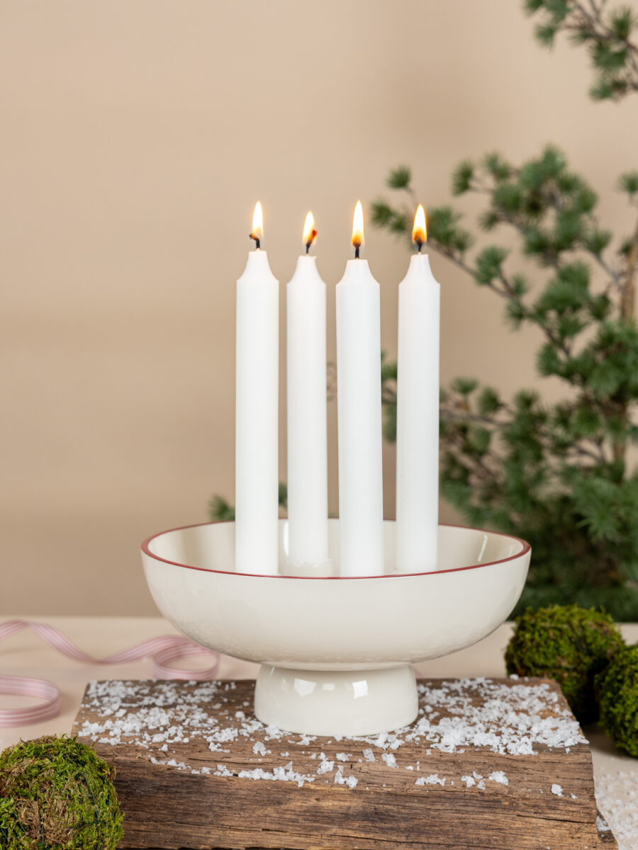 Osläckt vit adventsljusstake på fot i keramik med tunn röd kant, Granhammar Jubileum, stilrent placerad på ett ljust träbord.