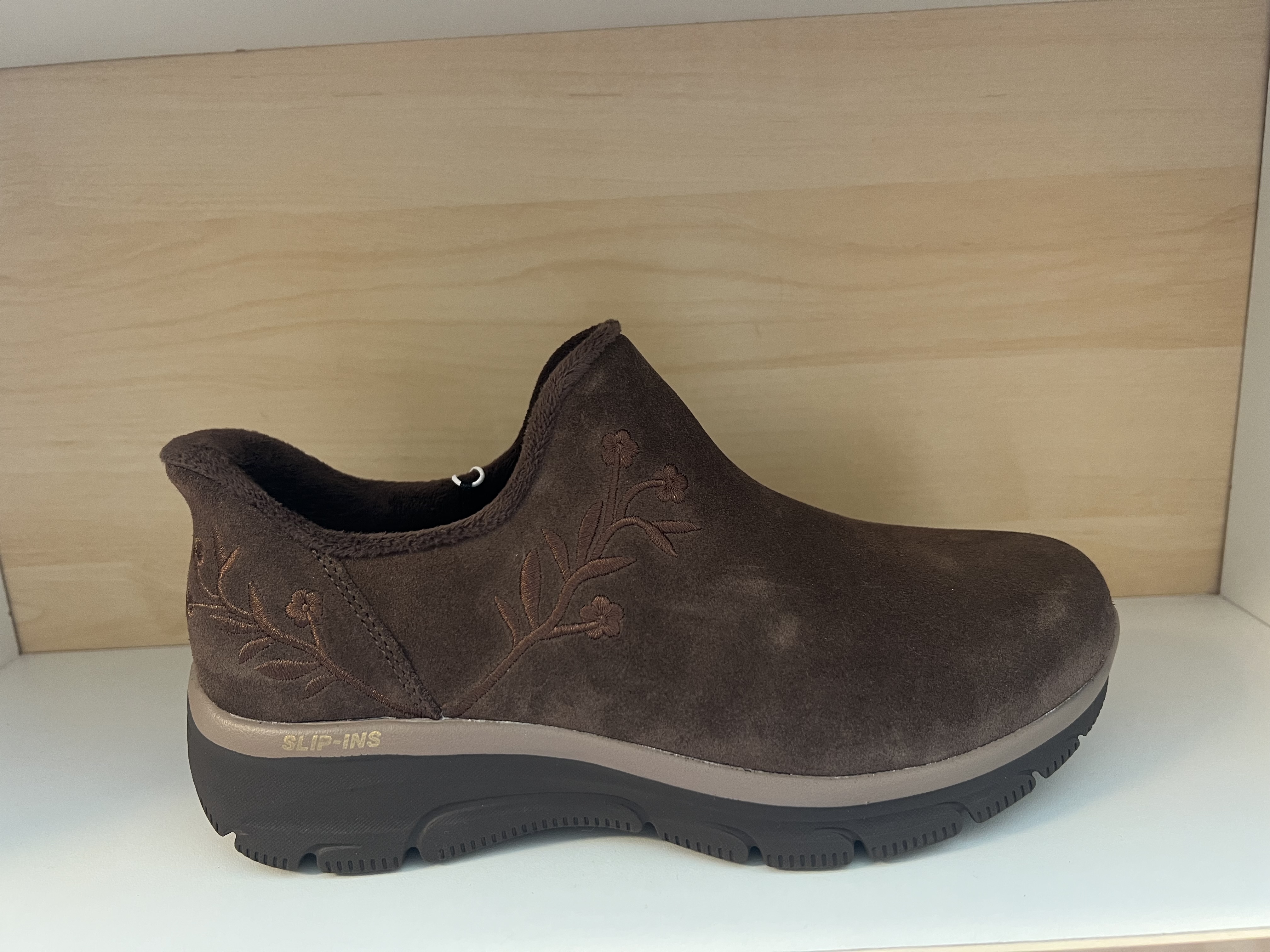 Skechers Damkänga i brunt Scotchgard-behandlad mocka med broderat blommotiv. AirCooled, Memory Foam innersula. Fodrad. Relaxed Fit=Bredare både på höjden och bredden framme vid tårna. Slip-Ins.