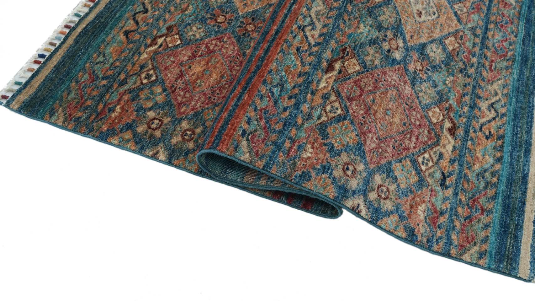 Detaljbild av Samarkand Blå 101x154 cm med uppvikt kant som visar mattans baksida, täta handknytning och mönstrade ullugg.