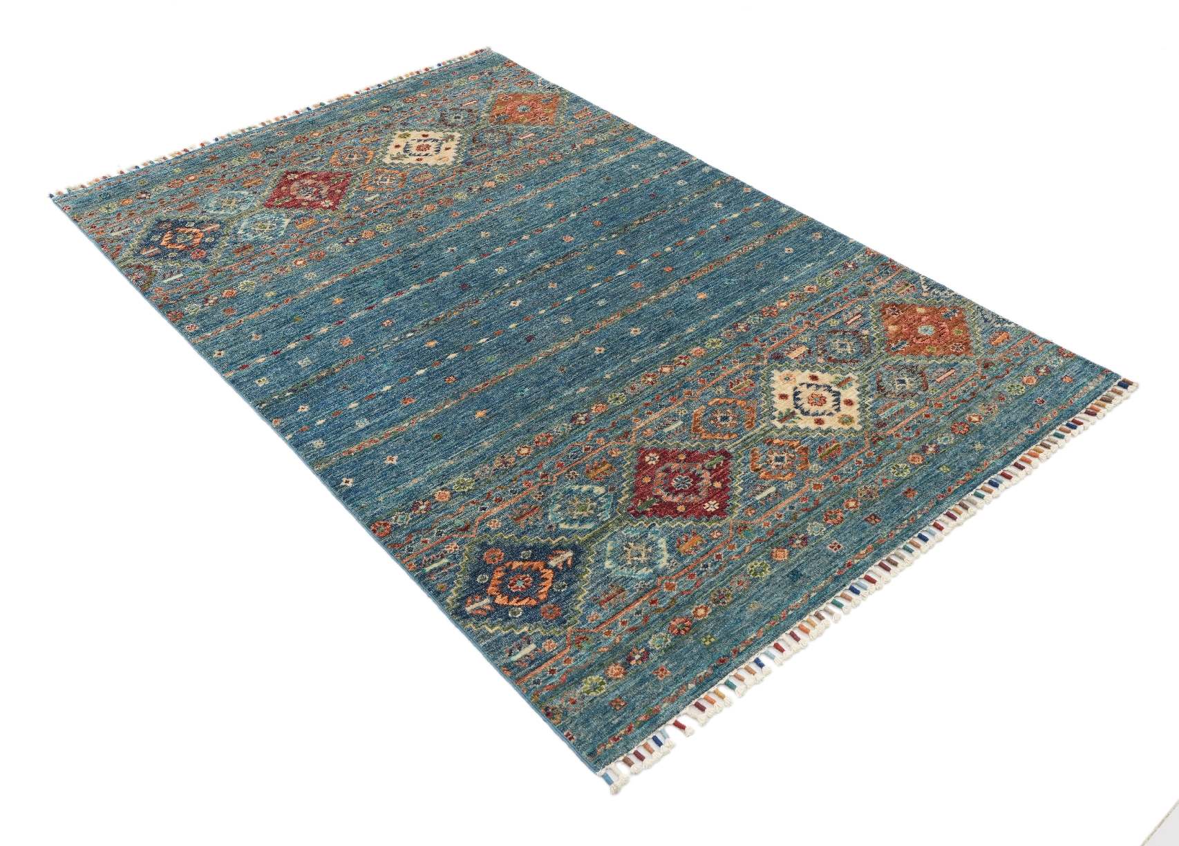 Produktbild i vinkel av Samarkand Blå 120x182 cm, handknuten ullmatta med melerad blå botten och färgstarka medaljonger.