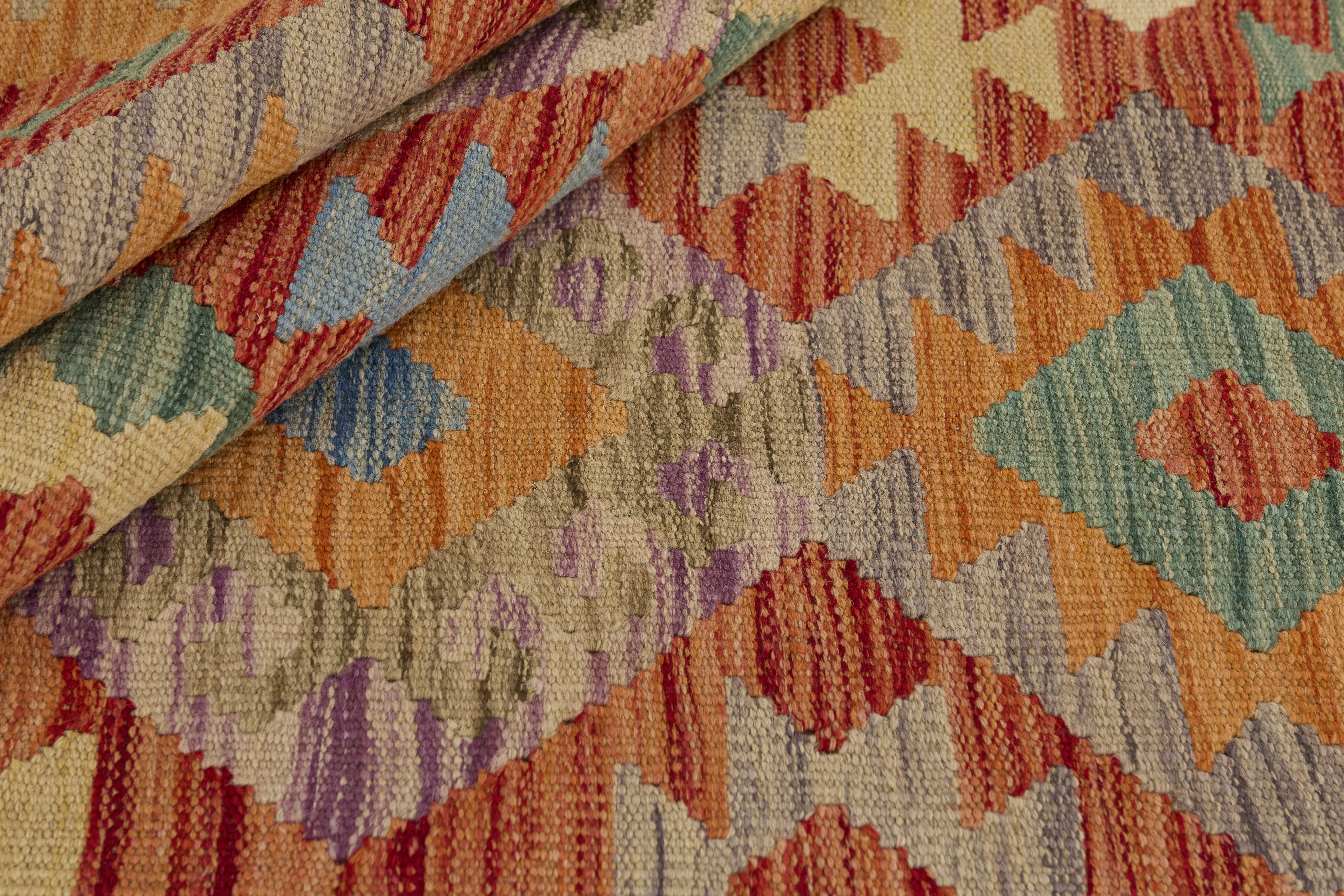 Närbild av Kelim 124x176 cm där mattan är vikt för att visa den handvävda ullstrukturen och geometriskt mönster i terrakotta, blått, grönt och lila.