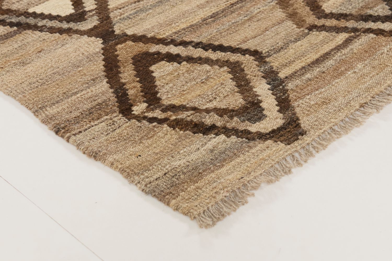 Detaljbild av Kelim 180x240 cm som visar mattans hörn med naturliga ullfransar, den handvävda strukturen och det mörkbruna rombmönstret mot en melerad beige botten.