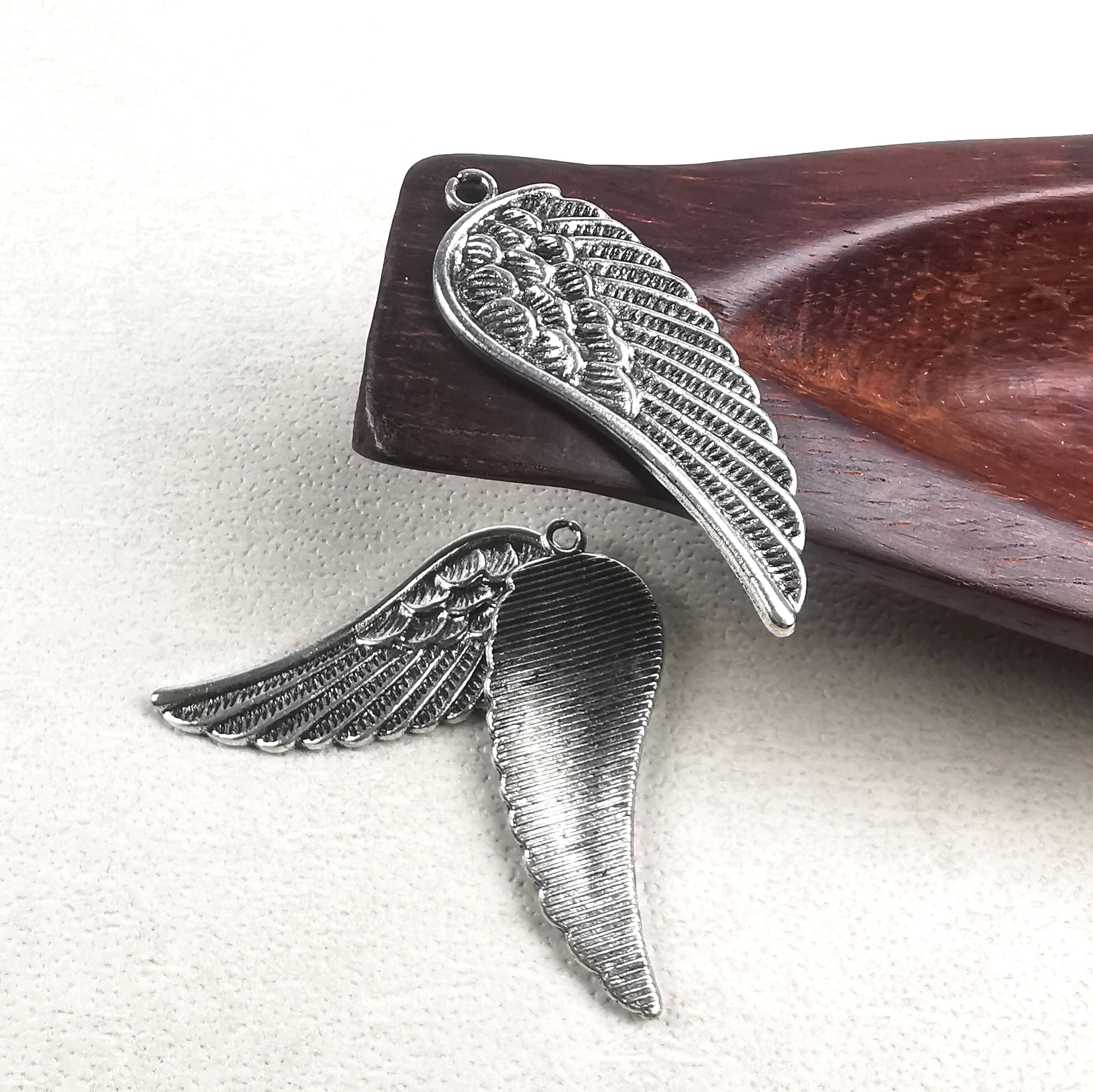 Tre antiksilverfärgade vingeberlocker i metall, cirka 15×44 mm med 2,5 mm hål, visade mot ljus bakgrund.