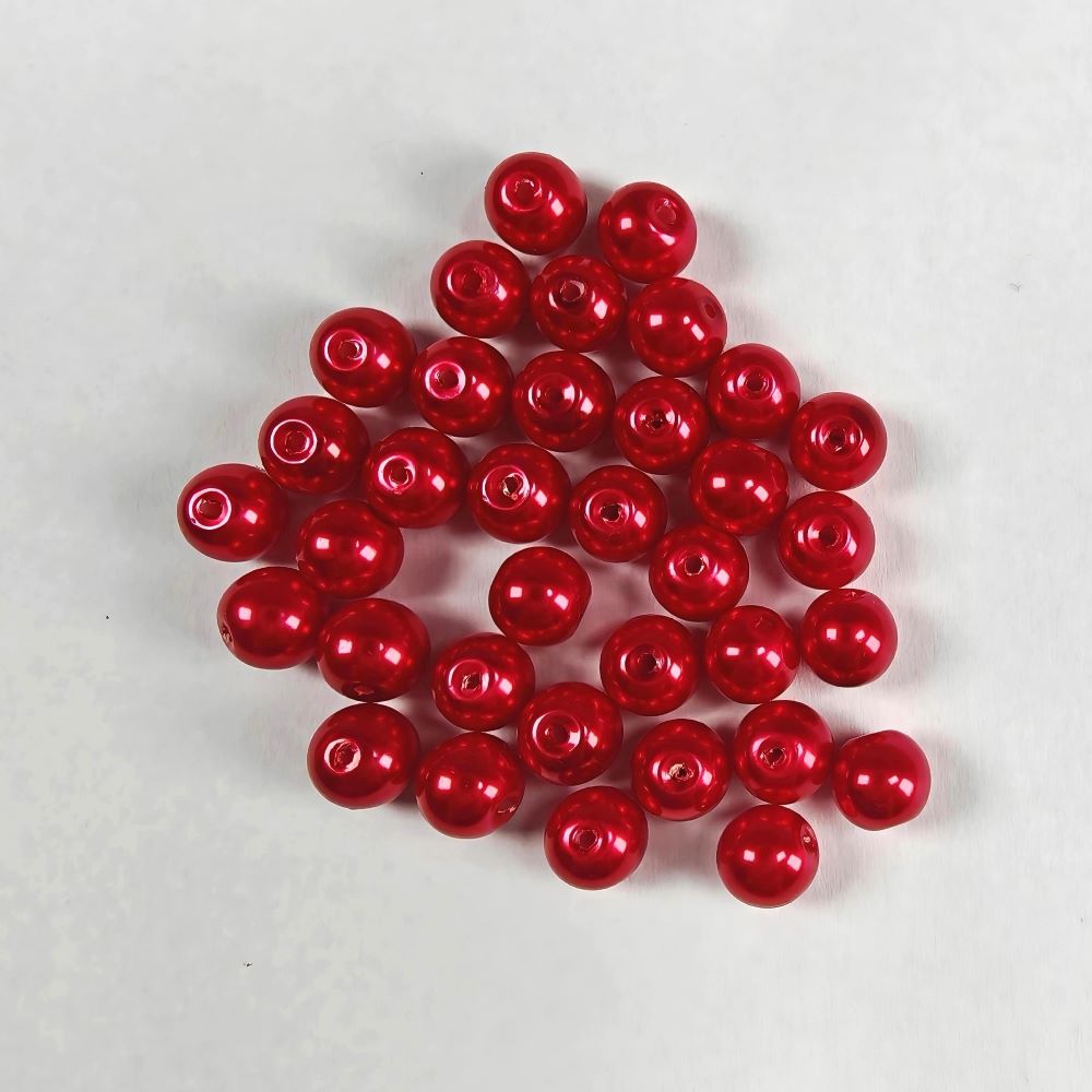 Röda vaxade glaspärlor 8 mm med cirka 1 mm hål, cirka 30 stycken visade i närbild mot grå bakgrund.