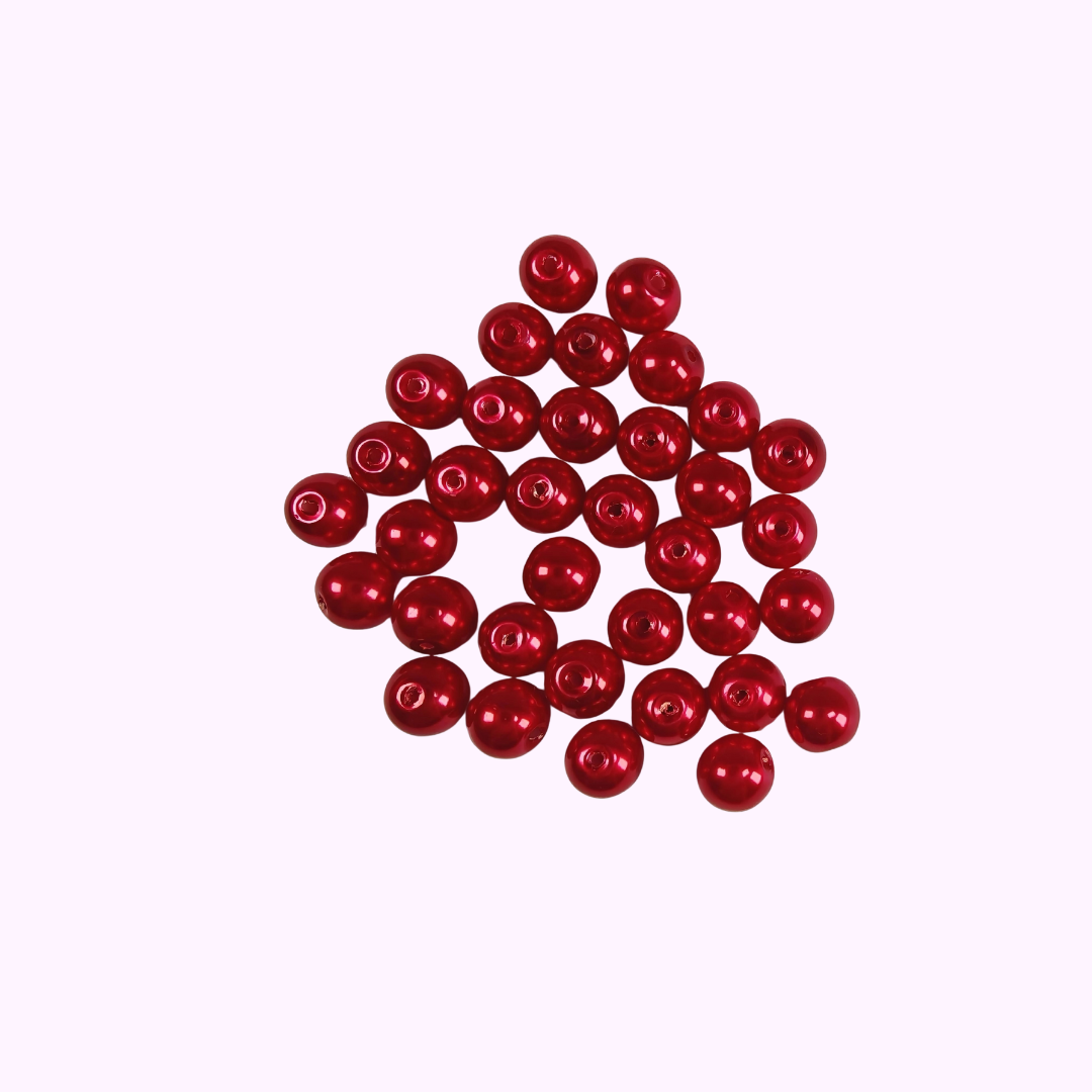 Röda vaxade glaspärlor 8 mm med cirka 1 mm hål, cirka 30 stycken visade i närbild mot rosa bakgrund.