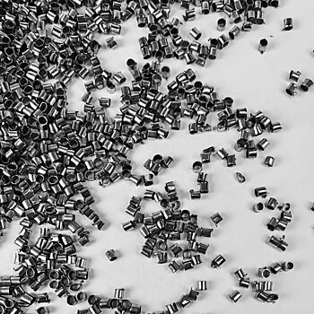Tubformade klämpärlor i antiksilverfärg, ca 1,5 mm stora med 1 mm hål, visade i närbild