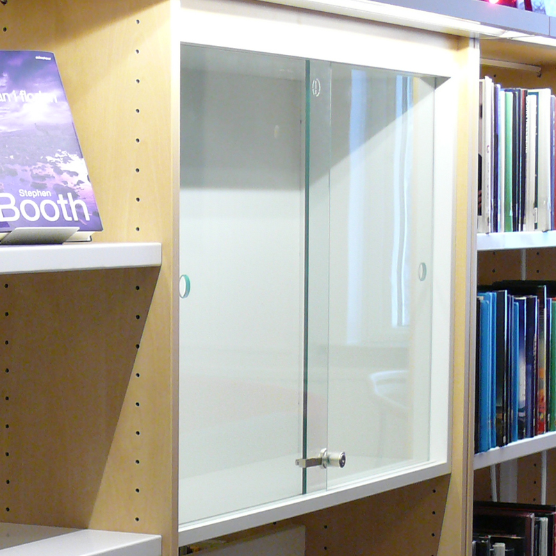 Vitrineskab/montréskab med låsbare glasskydelåger og én glashylde, integreret i hyldesektion og tilpasset BK Librarys hyldesystemer.
