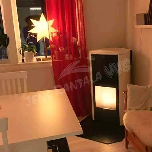 Pelletskamin Lilla Frö. Vit med svart front. Monterad i ett hörn. Röda gardiner och julstjärna i fönstret.
