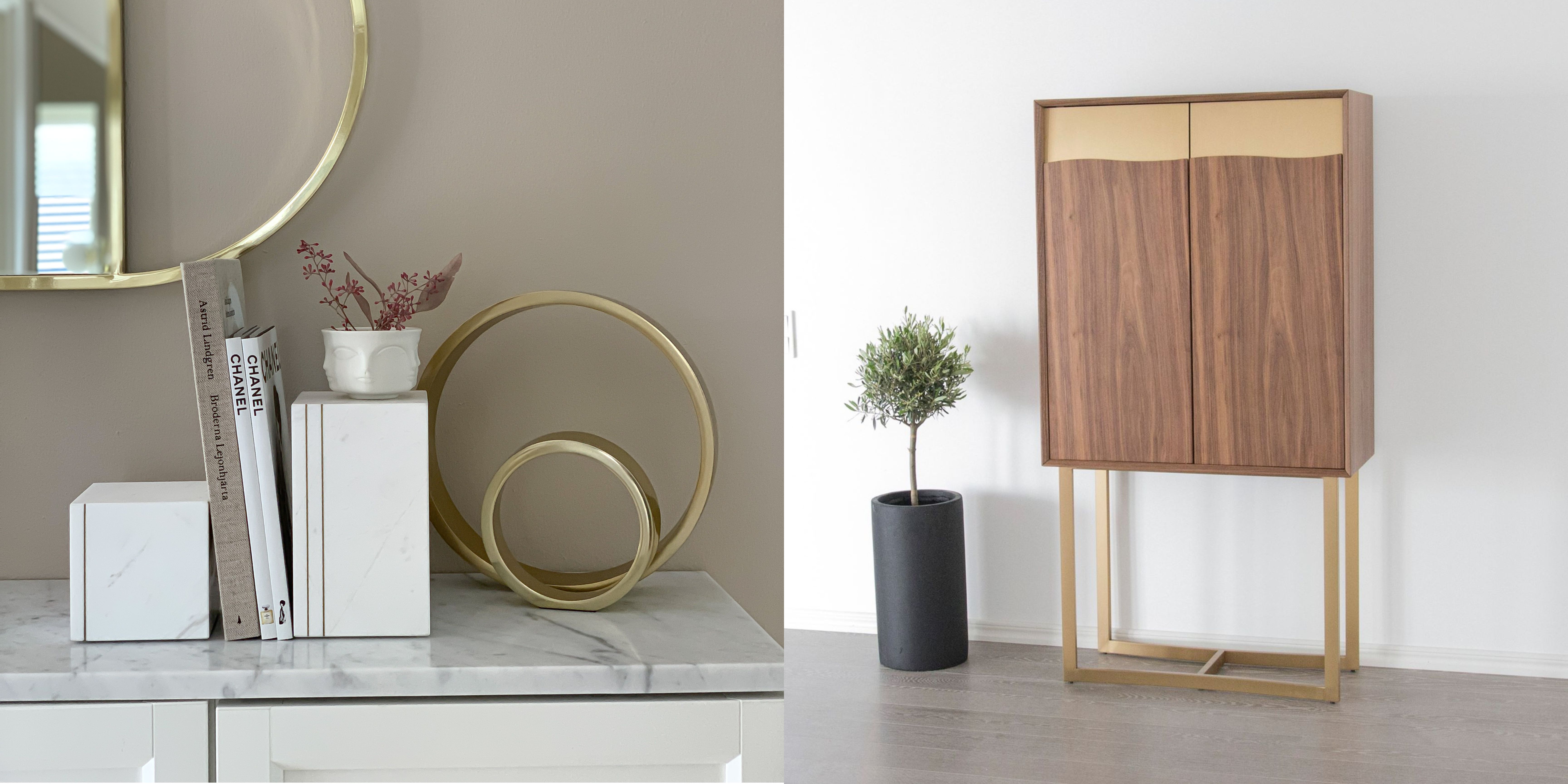 Marmorbokstöd i vit marmor med flera inredningsböcker och en rund spegel i mässing ovanför mot en beige vägg samt ett barskåp i ljus valnöt och mässingsdetaljer och mässingsben med hyllor på insidan för vinhållare stående mot en vit vägg