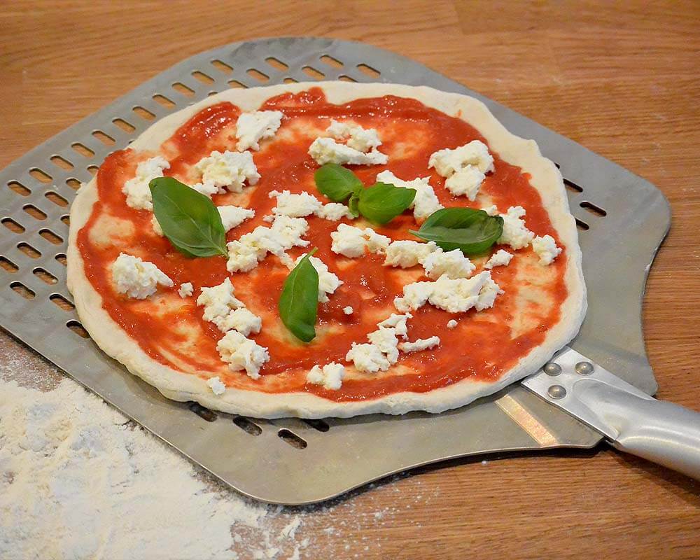 En ubagt pizza med forskellige toppings ligger på et melet træbord.