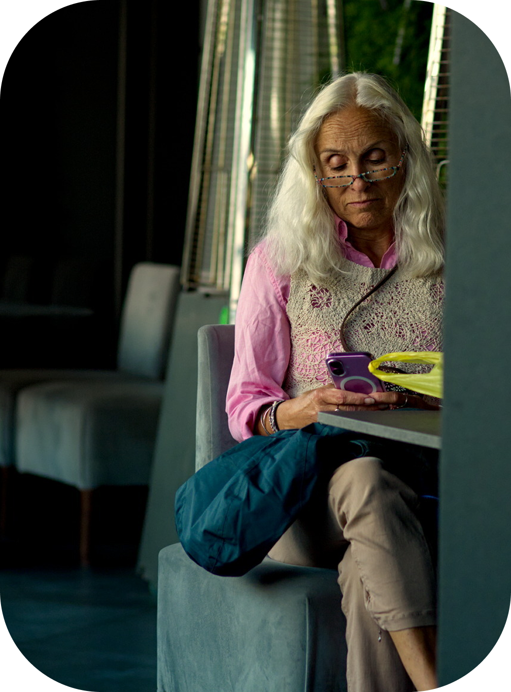 An older woman sitting on a sofa, looking down at her mobile phone.