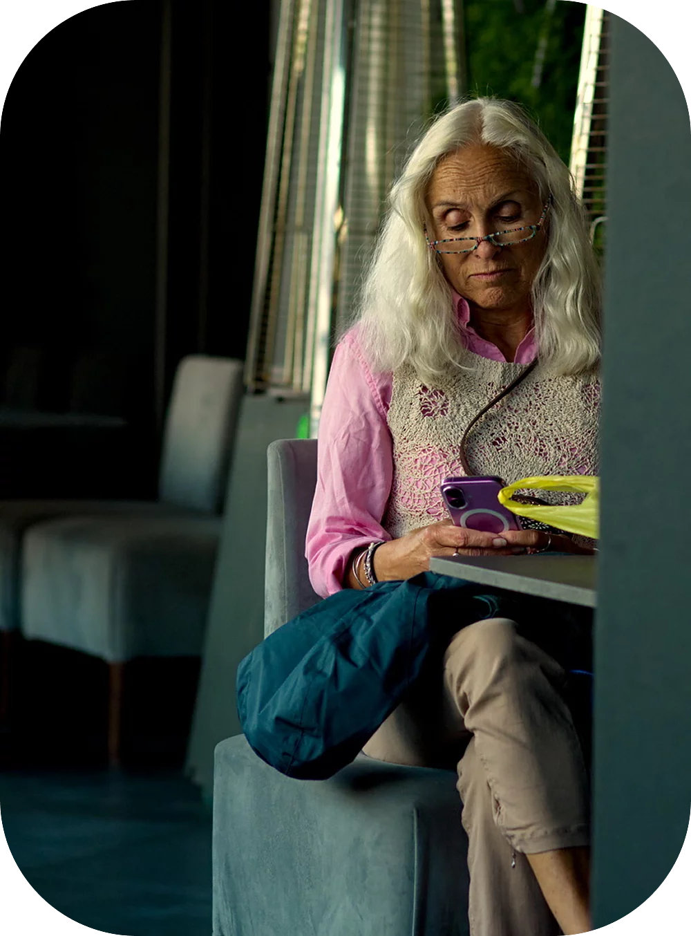 An older woman sitting on a sofa, looking down at her mobile phone.