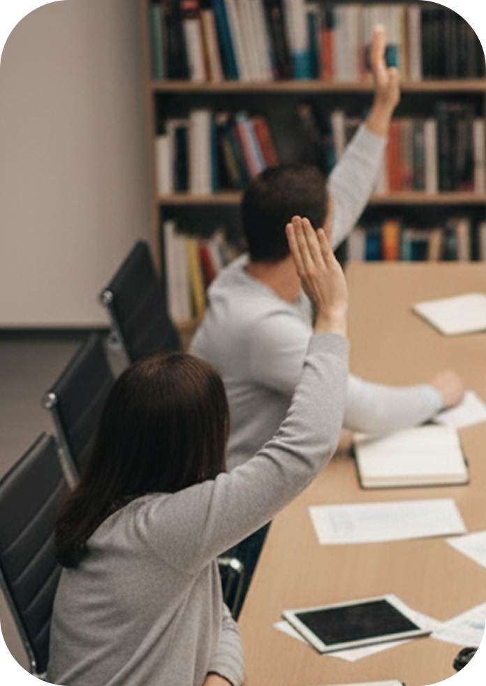 A woman and a man in a conference room raising their hands, symbolizing ‘I want to be part of this.’